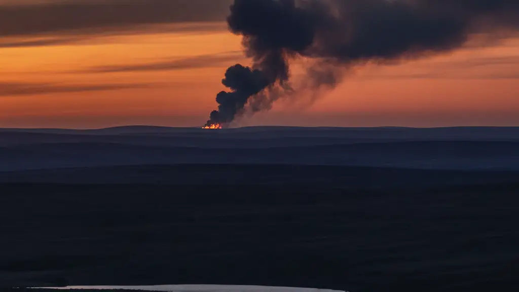Distant smoke plume over dark moorland with reservoir water reflecting dramatic sky.