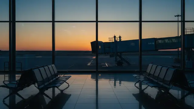An empty airport departure gate and disconnected jet bridge at sunset.