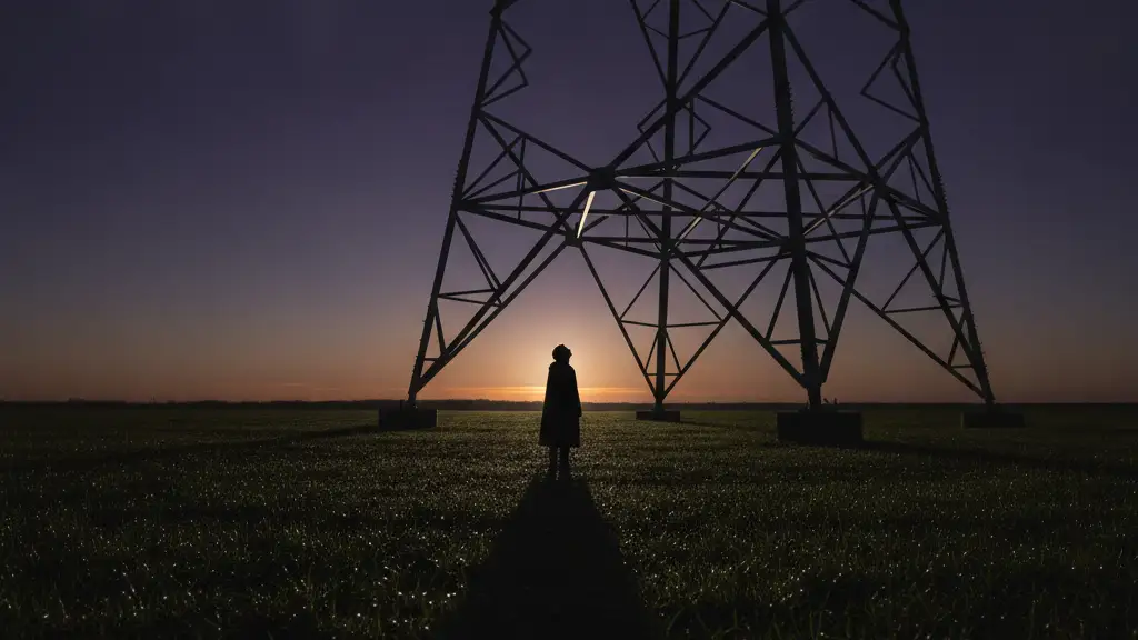 Silhouetted figure looking up at a new electricity pylon in a field at dusk.
