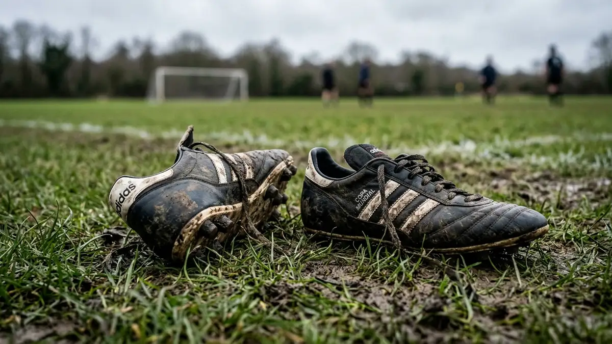Muddy football boots on a grassy pitch, one askew, with a blurred background.
