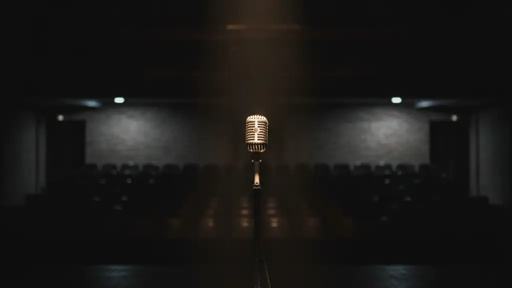A lone microphone on a dark, empty stage under a single spotlight.