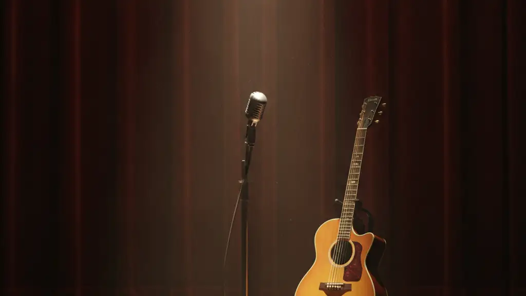 Empty stage with a single microphone and acoustic guitar under a spotlight.