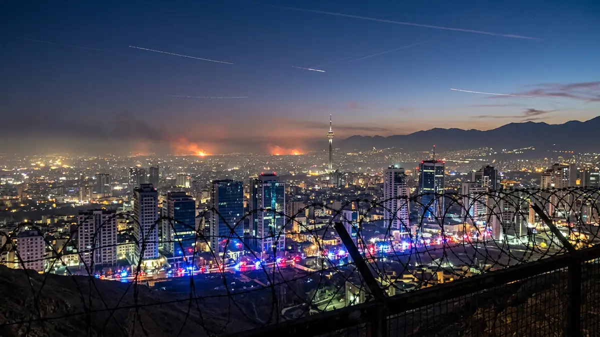 Tehran skyline at dusk with emergency light reflections and jet contrails in the sky.