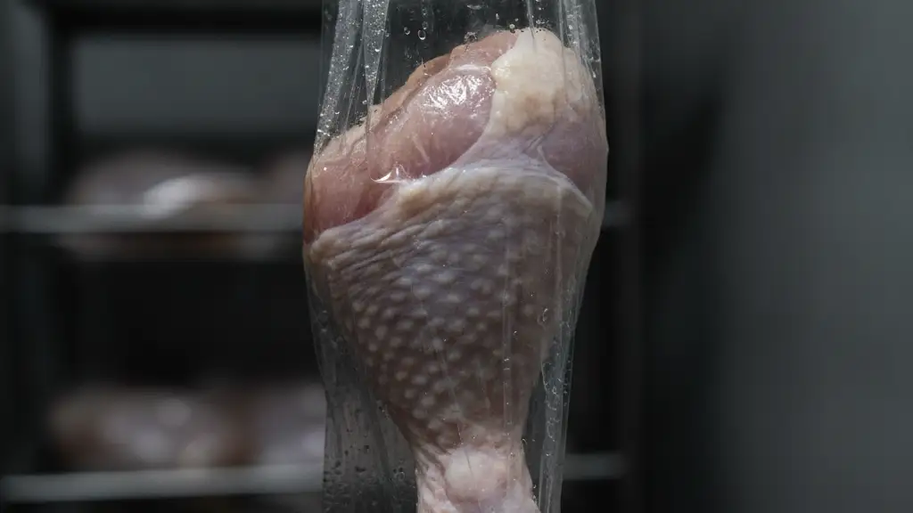 Close-up of a raw chicken drumstick in plastic packaging, with blurred industrial background.
