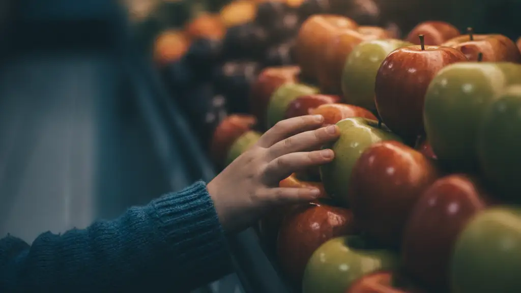 Child's hand reaching for apples in a grocery store produce section.