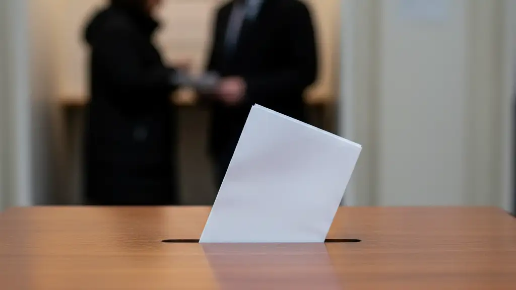 A close-up of a ballot paper being inserted into a wooden voting box slot.