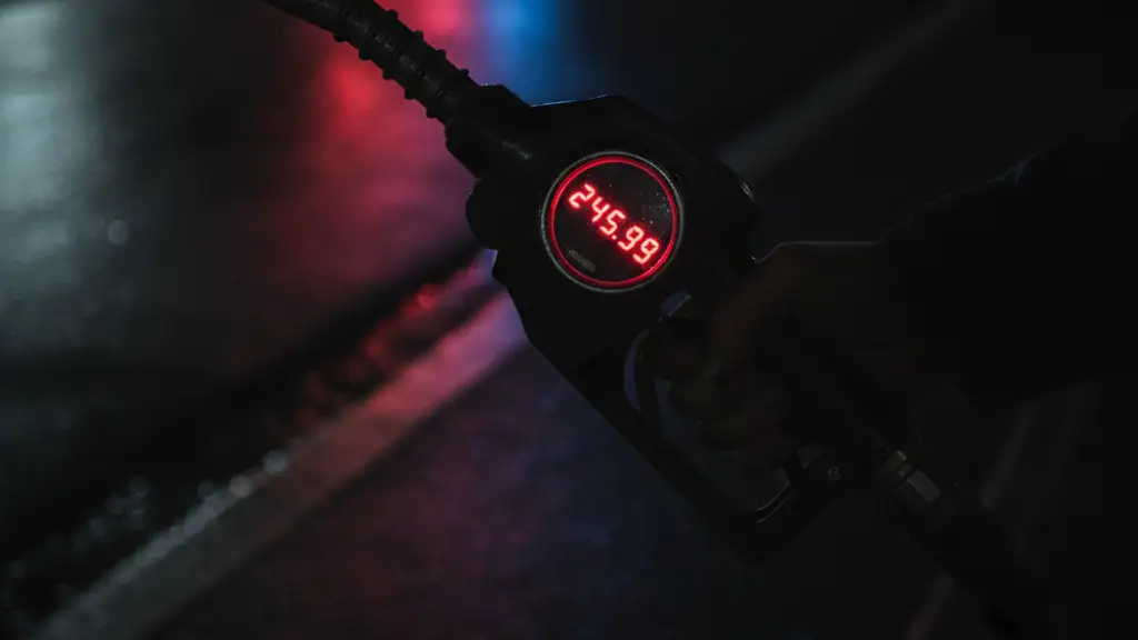 Silhouetted hand holding a petrol pump nozzle, high price display, emergency light reflections.