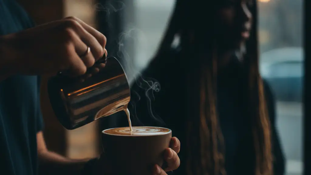 Blurred silhouette of a young person watching a barista's hands making coffee.