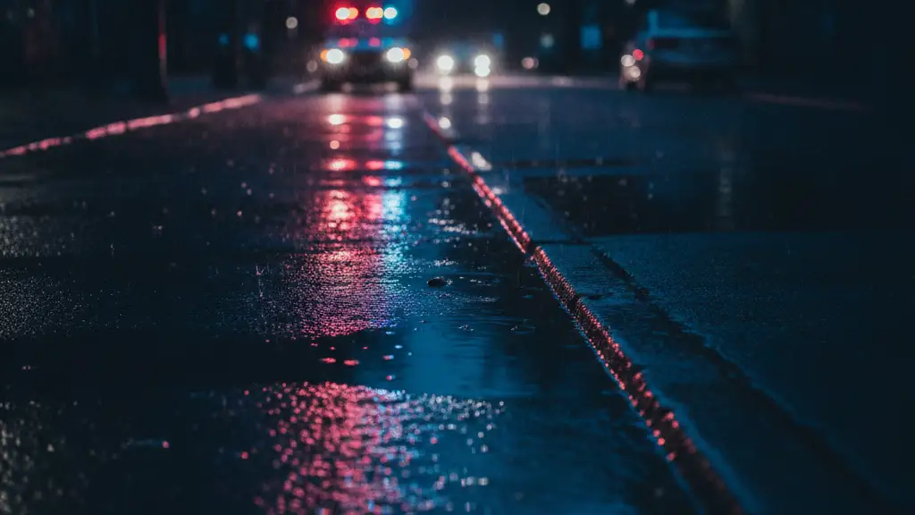 Red and blue emergency lights reflecting in a rain puddle on a dark street.