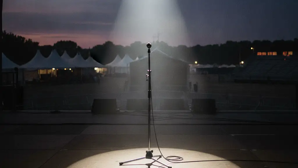 An empty microphone stand under a single spotlight on a dark festival stage.