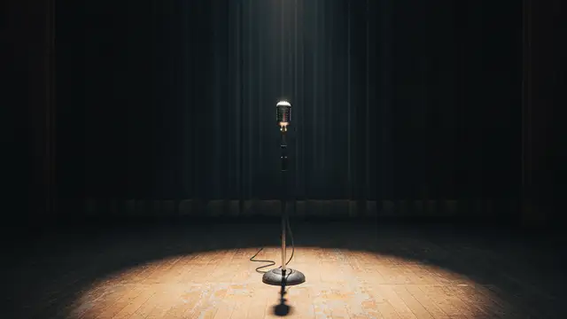A lone microphone stand on an empty, dimly lit stage under a single spotlight.