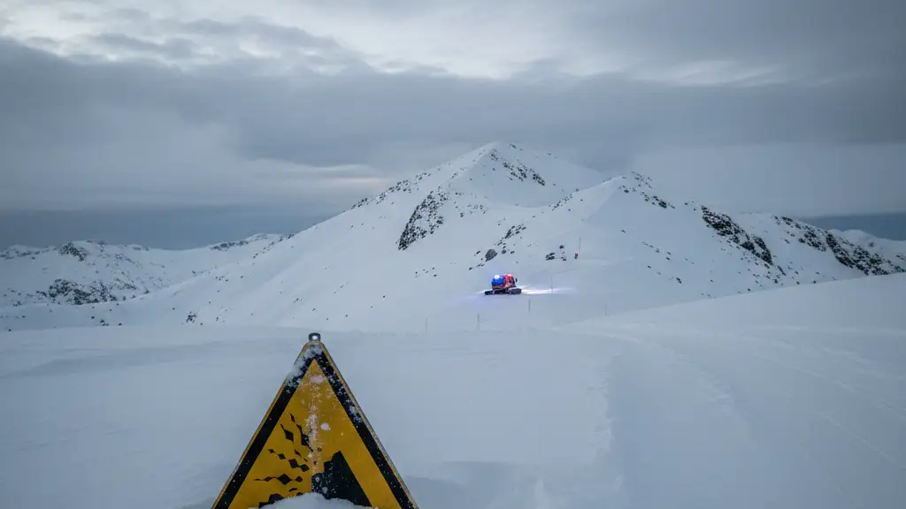 An avalanche warning sign on a snowy mountain slope with emergency lights in the distance.