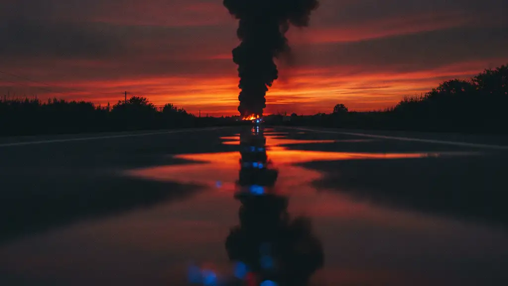 Ominous smoke plume at sunset, emergency lights reflecting in a puddle.