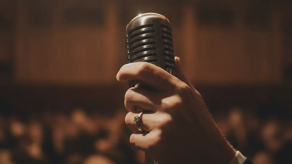 A close-up of a hand holding a microphone, a wedding ring visible.