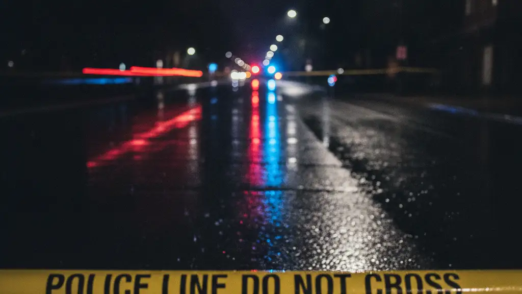 Police line tape reflecting emergency lights on a wet road at night.