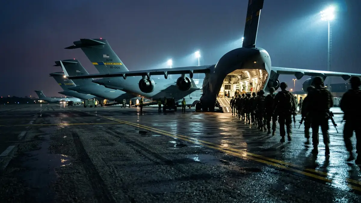 Silhouetted soldiers boarding a military transport plane on a wet airfield at night.