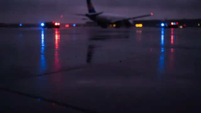 Emergency lights reflecting on wet tarmac with a distant airplane tail.