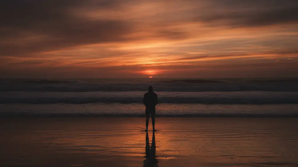 Silhouetted lifeguard on beach at sunset, looking at turbulent ocean.