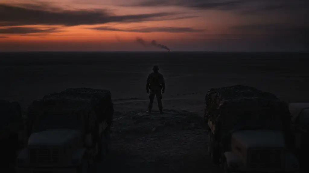 Silhouetted soldier overlooking a desert landscape with distant smoke plume.