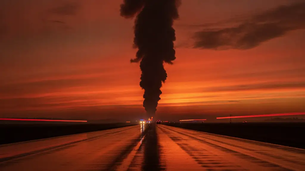 Thick smoke plume against a fiery sunset, emergency lights reflecting on a wet road.