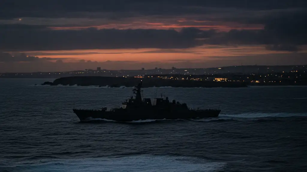 Silhouette of a warship on a dark, turbulent ocean near a distant coastline.