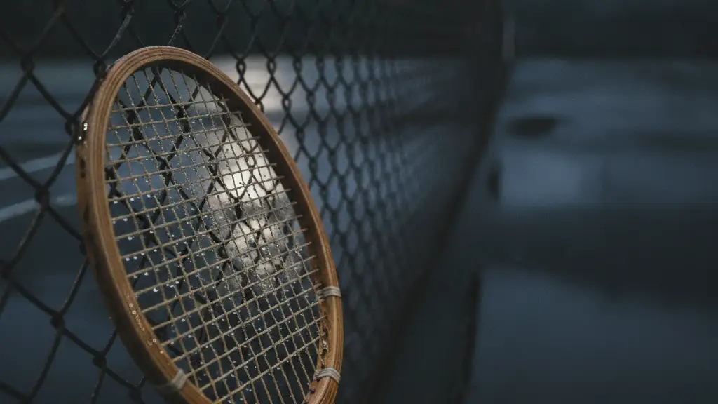 A tennis racket leans against a chain-link fence on a wet, deserted court at dusk.