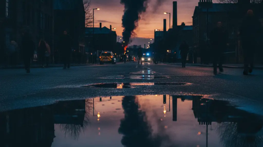 Emergency lights reflecting in a rain puddle with smoke rising in the distance.