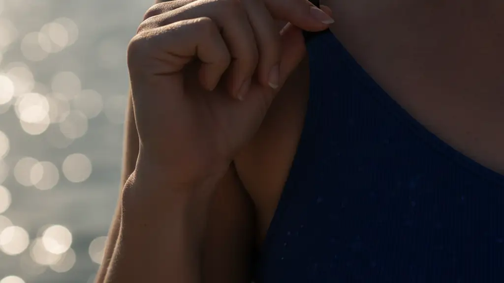 A woman's hand adjusting a wet swimsuit strap, water reflections in background.