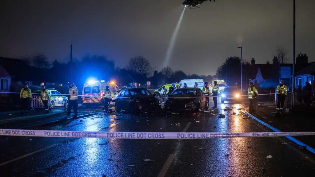 Emergency vehicle lights and police tape at the scene of a road collision at night.