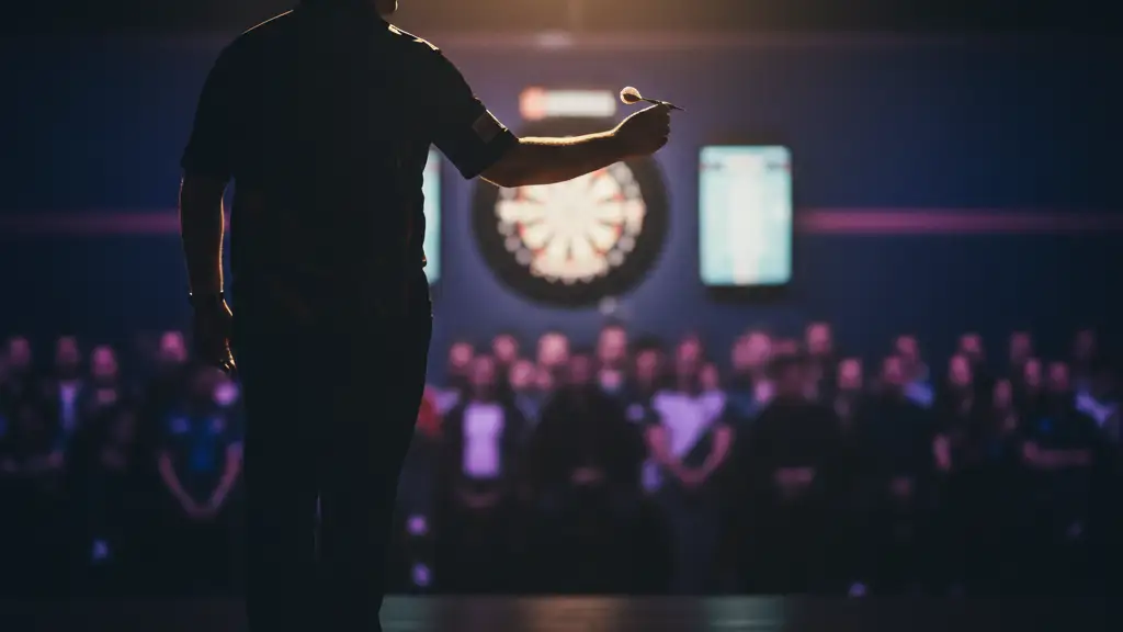 Silhouette of a darts player on stage, hand gripping a dart, under a spotlight.